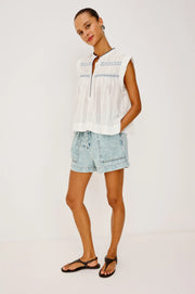 Woman wearing a flowy sleeveless white top with blue embroidery 