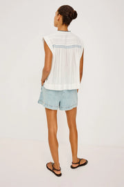 Woman wearing a flowy sleeveless white top with blue embroidery 