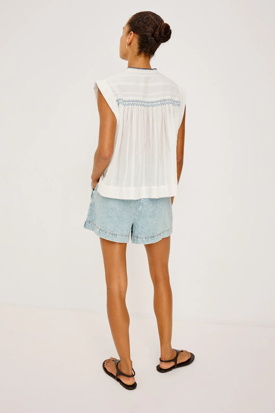 Woman wearing a flowy sleeveless white top with blue embroidery 