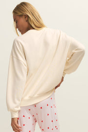 A woman wearing an off white crewneck sweatshirt with the word  “LOVER” written in pink chenille, back view