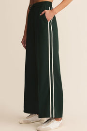 Dark green pants with white stripes worn by a person on a beige background