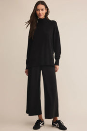 Woman wearing a black turtleneck and wide-leg pants on a beige background