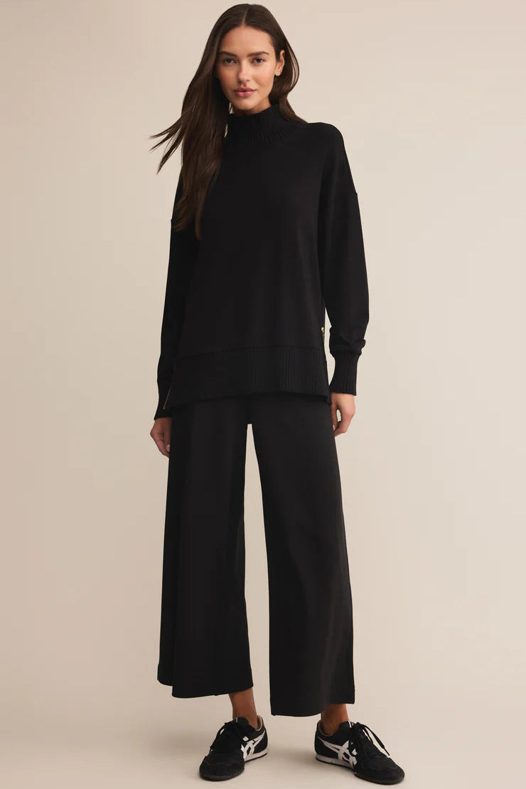 Woman wearing a black turtleneck and wide-leg pants on a beige background