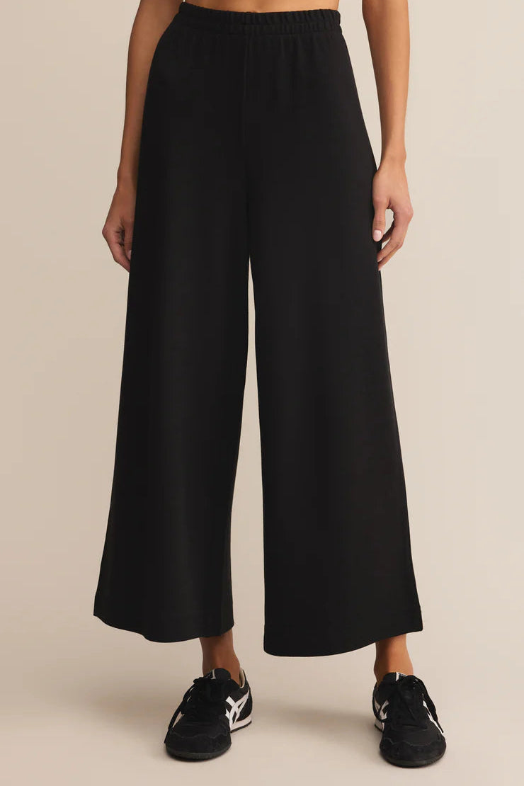 Person wearing black wide-leg pants on a beige background