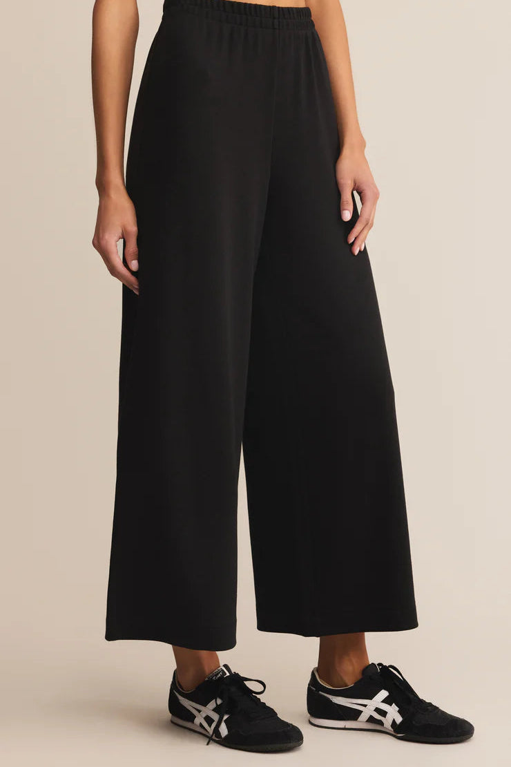 Person wearing black wide-leg pants on a beige background