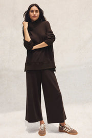 Woman wearing a brown outfit with wide-leg pants on a light background