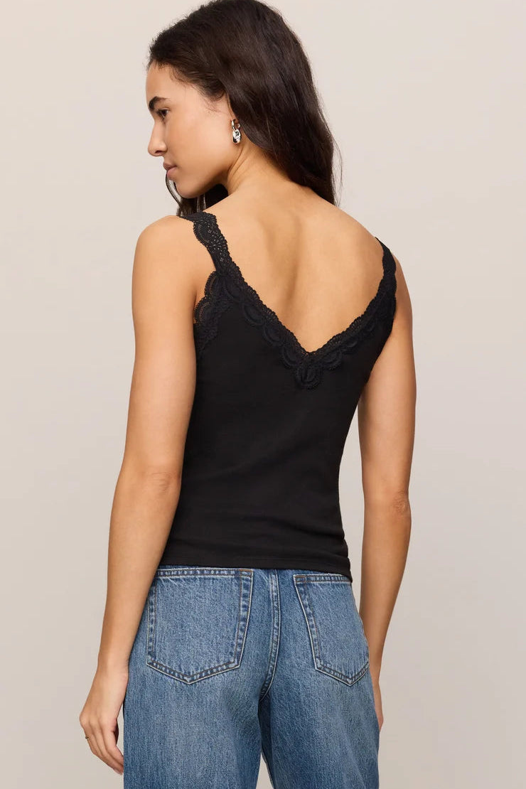 A woman shown from the back wearing a black lace-trimmed tank top and blue jeans against a plain light gray studio background.
