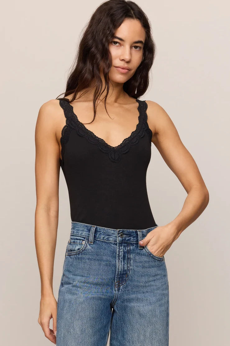 Woman wearing a black tank top with lace details and blue jeans on a beige background
