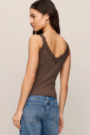 Woman wearing a brown tank top with lace details and blue jeans on a beige background