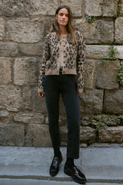 Woman wearing a leopard print cardigan against a stone wall.