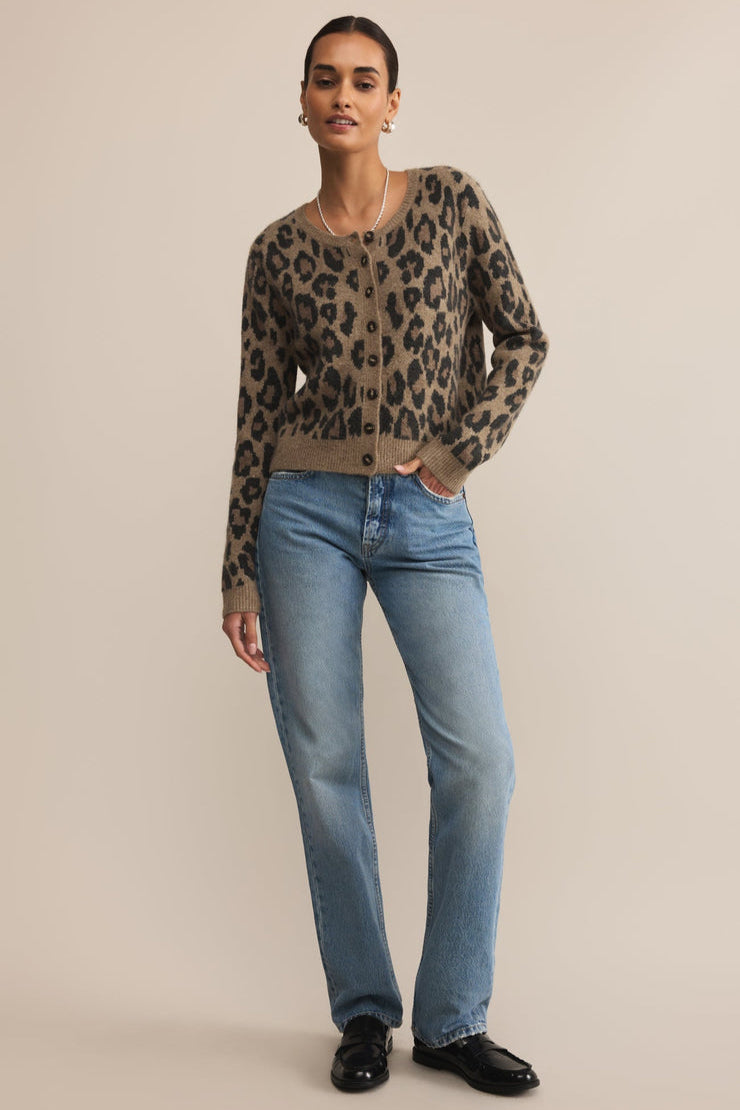 Woman wearing a leopard print cardigan, light blue jeans, and black shoes on a beige background