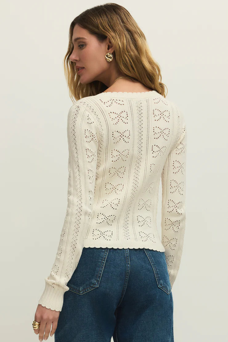 Woman wearing a cream cardigan with buttons on the front, scalloped trim and openwork detailing, back view