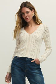 Woman wearing a cream cardigan with buttons on the front, scalloped trim and openwork detailing, front view