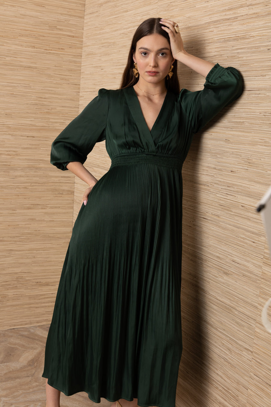 A woman wearing a dark green pleated midi dress with three-quarter sleeves and a V-neckline
