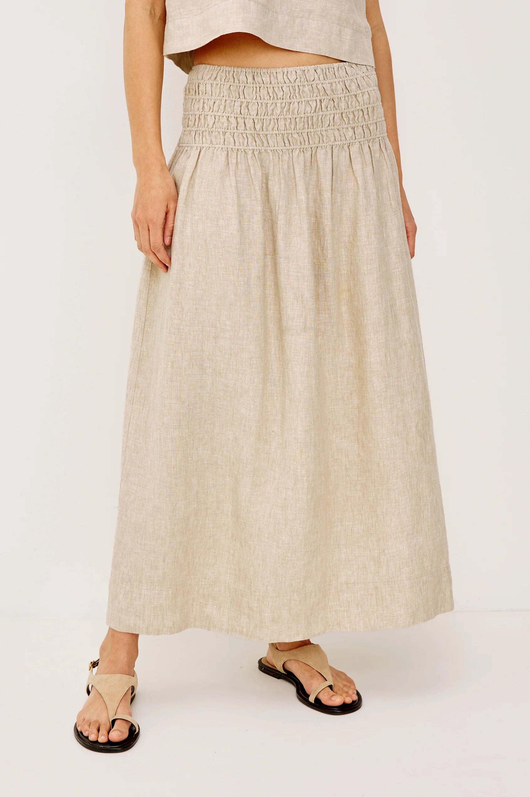 Woman wearing a beige linen midi skirt with a smocked elastic waistband, front