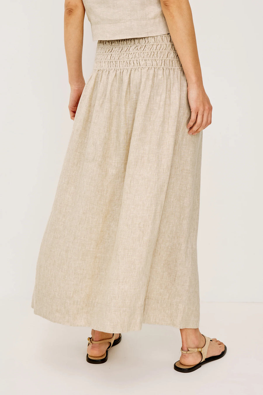 Woman wearing a beige linen midi skirt with a smocked elastic waistband, back