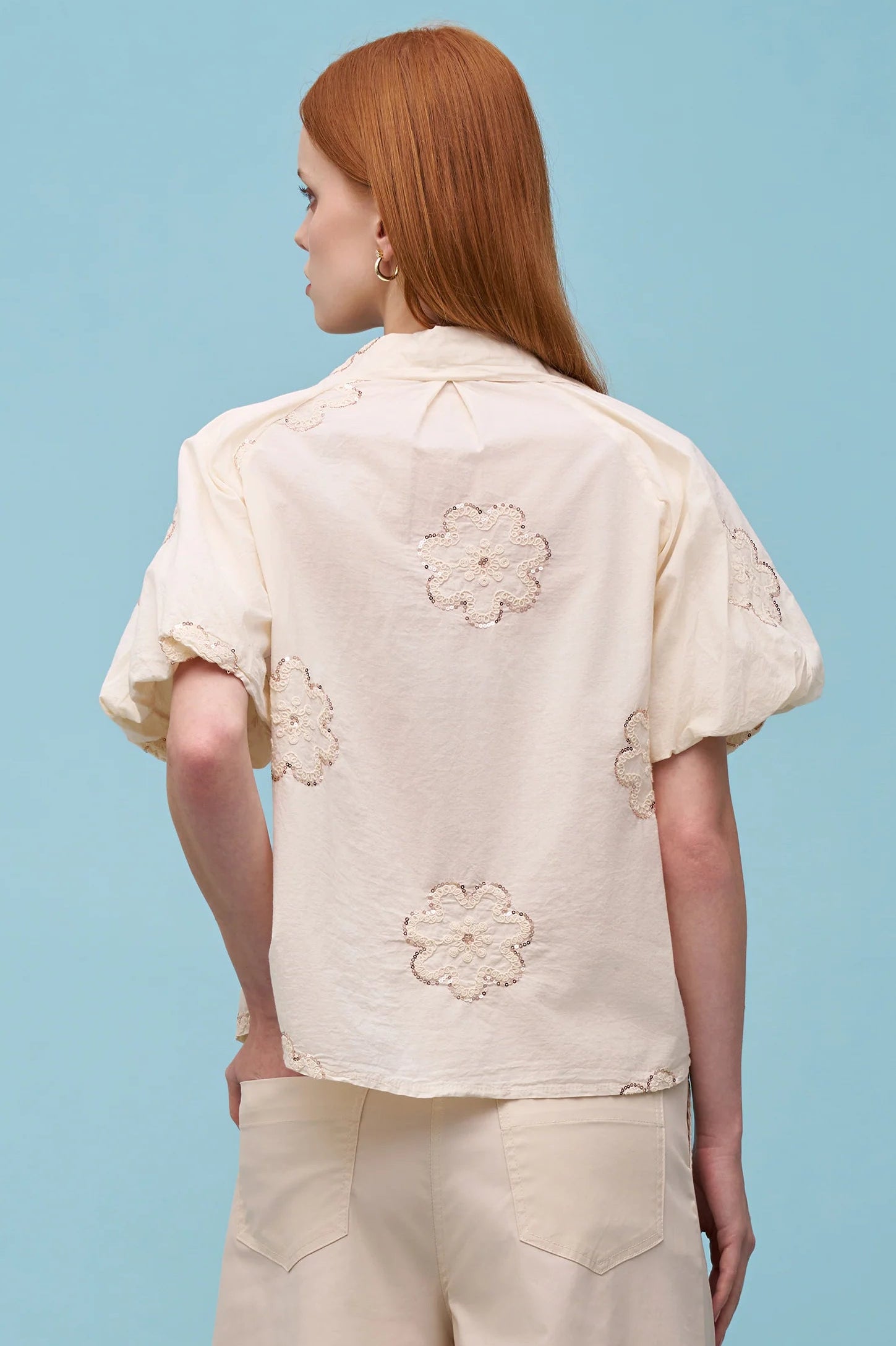 Woman wearing a cream short-sleeve button-up blouse with delicate floral embroidery and a pointed collar, front