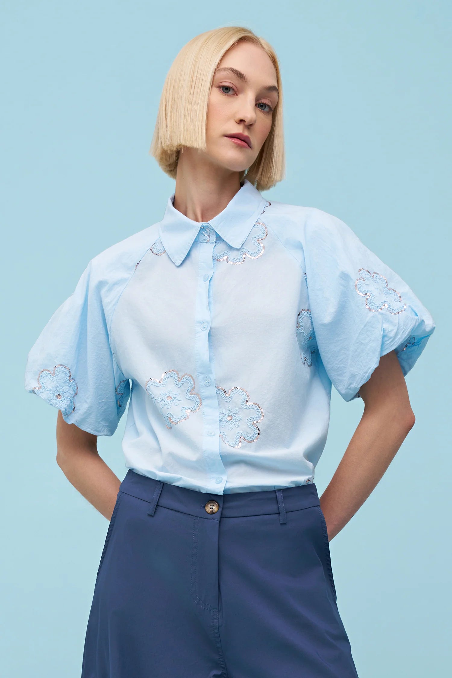 Woman wearing a light blue short-sleeve button-up blouse with floral embroidery and a pointed collar, front view
