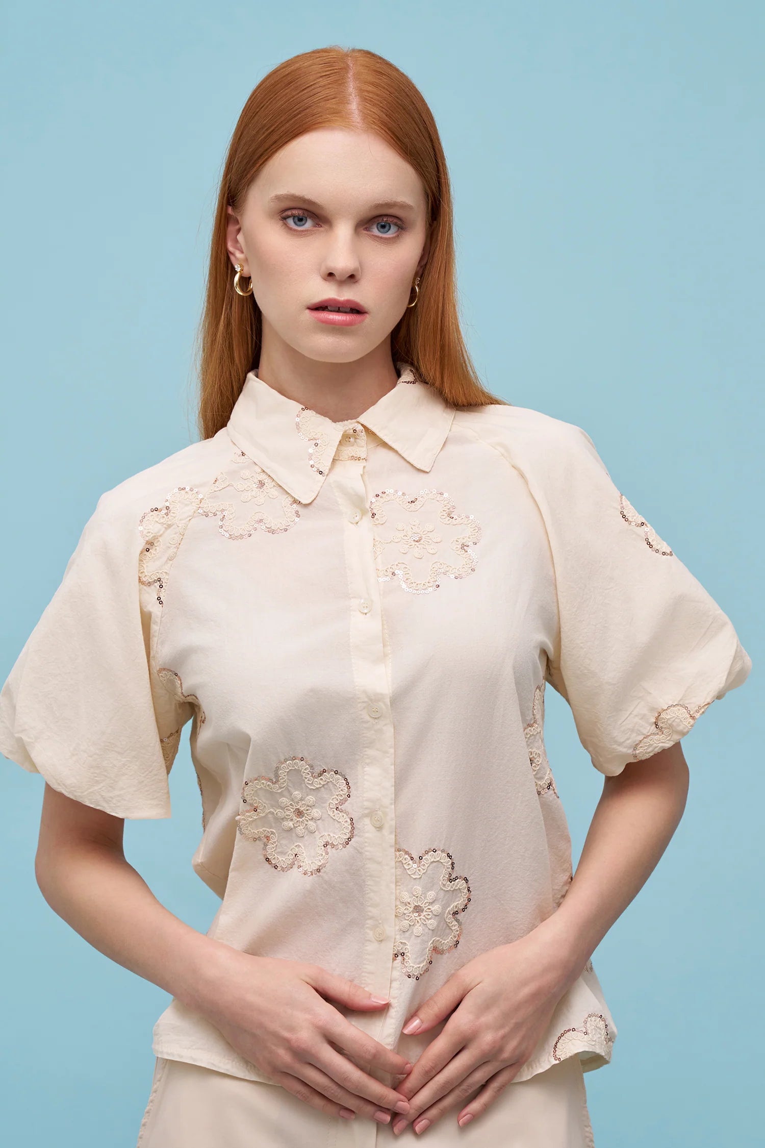 Woman wearing a cream short-sleeve button-up blouse with delicate floral embroidery and a pointed collar, front