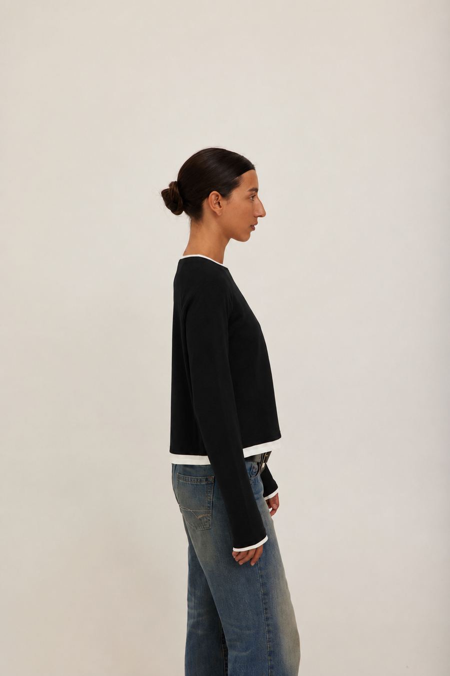 A model wearing a black long-sleeve crewneck sweater with white ribbed trim at the collar, cuffs, and hem. 