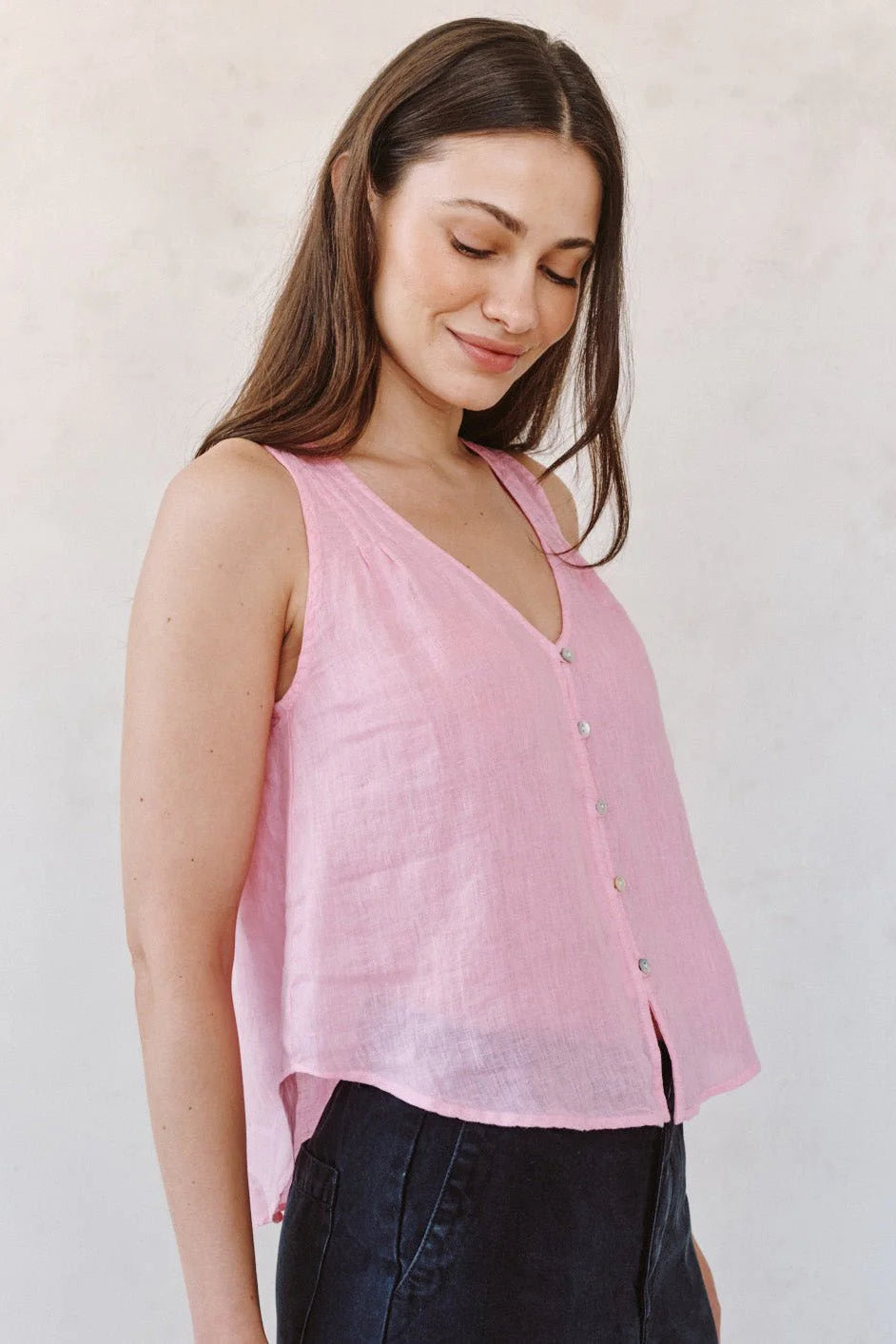 Woman wearing a pink sleeveless V-neck button-front blouse, side view