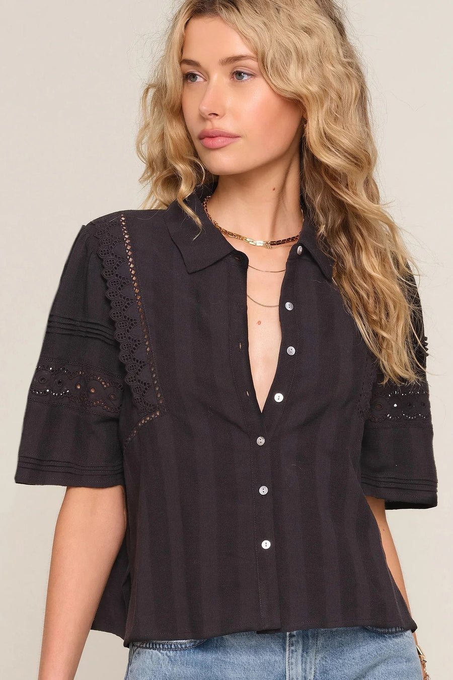 woman wearing a black short-sleeve button-front blouse with delicate lace inset detailing and a relaxed fit, front