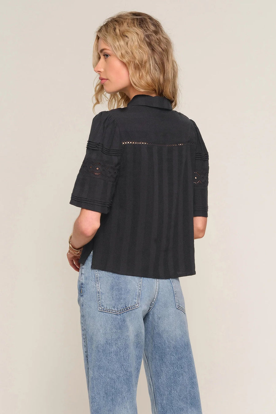woman wearing a black short-sleeve button-front blouse with delicate lace inset detailing and a relaxed fit, back