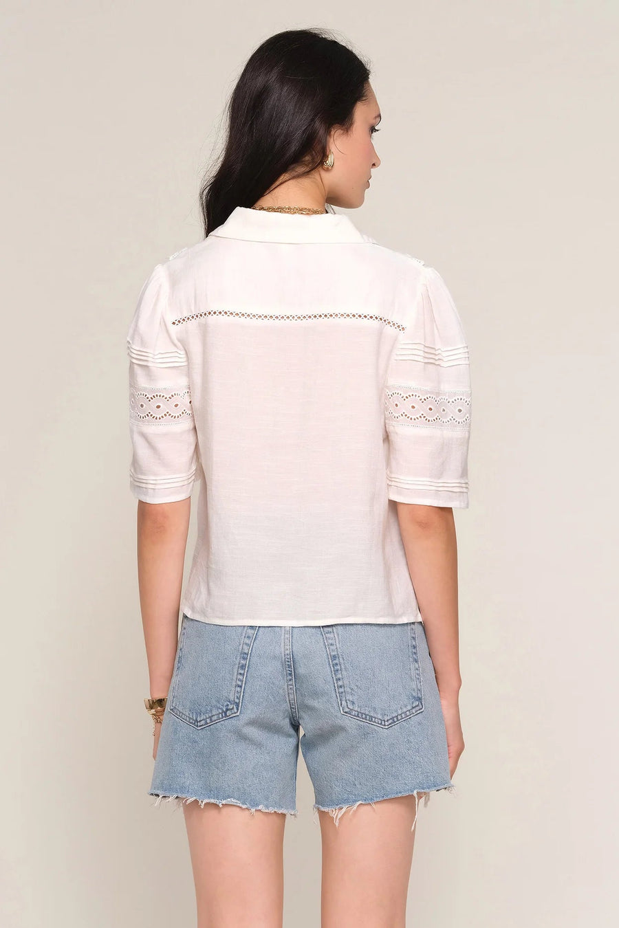 Woman wearing a off white blouse with lace details, back