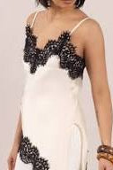 A woman wearing a white spaghetti-strap dress with black lace trim along the neckline and lower sides, photographed against a plain light background.