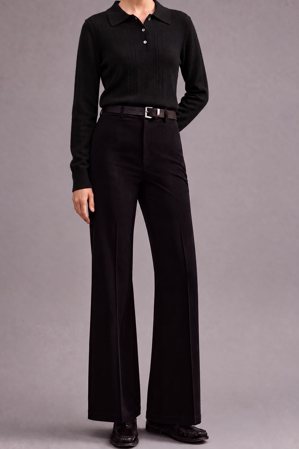 A model wearing a black long-sleeve ribbed knit polo shirt tucked into high-waisted black wide-leg trousers with a dark belt, standing against a solid gray studio background.