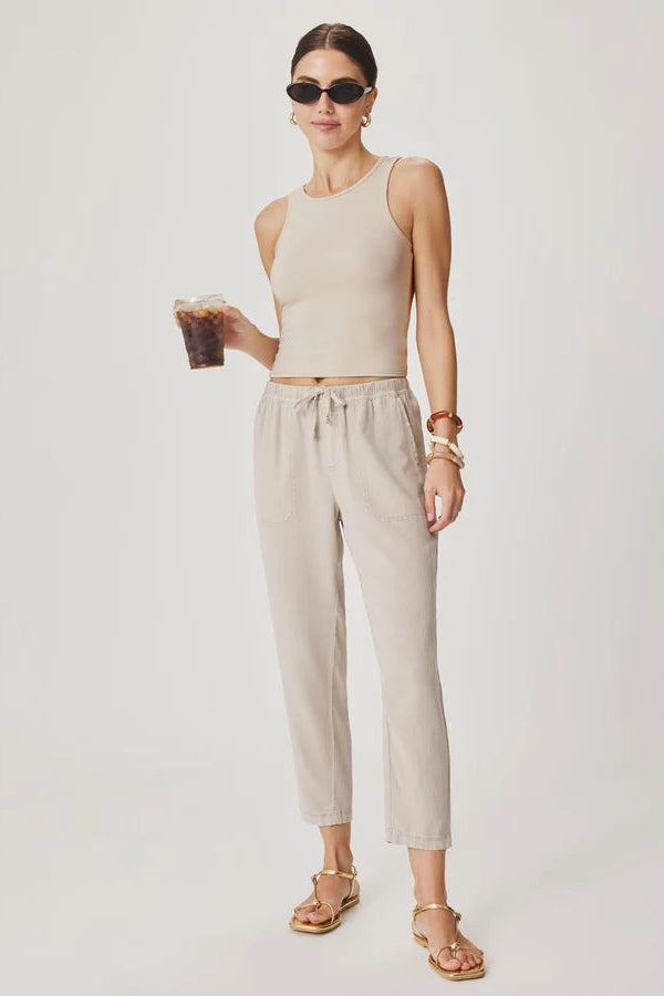 Woman wearing light beige cropped pull-on pants with an elastic drawstring waist, relaxed tapered fit, and front patch pockets, front