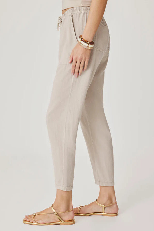Woman wearing light beige cropped pull-on pants with an elastic drawstring waist, relaxed tapered fit, and front patch pockets, side