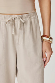 Woman wearing light beige cropped pull-on pants with an elastic drawstring waist, relaxed tapered fit, and front patch pockets, drawstring detail