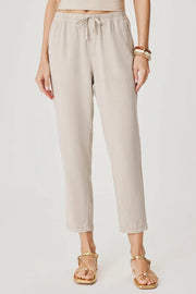 Woman wearing light beige cropped pull-on pants with an elastic drawstring waist, relaxed tapered fit, and front patch pockets, front