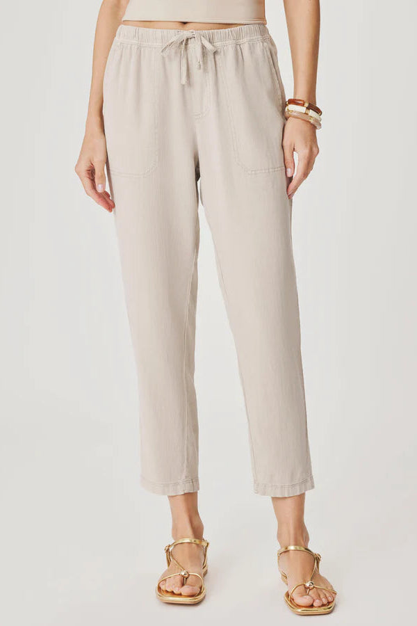 Woman wearing light beige cropped pull-on pants with an elastic drawstring waist, relaxed tapered fit, and front patch pockets, front