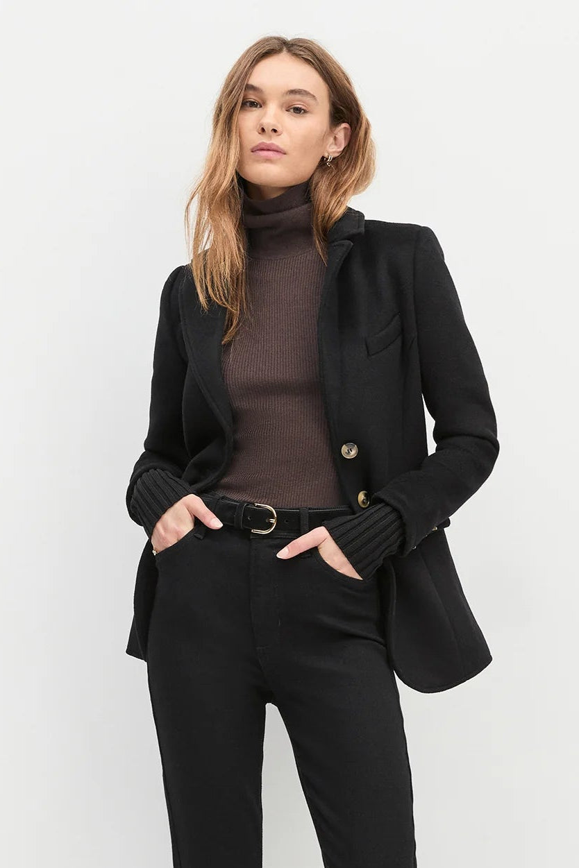 Woman wearing a black jacket with cuff sleeves, brown top and black jeans
