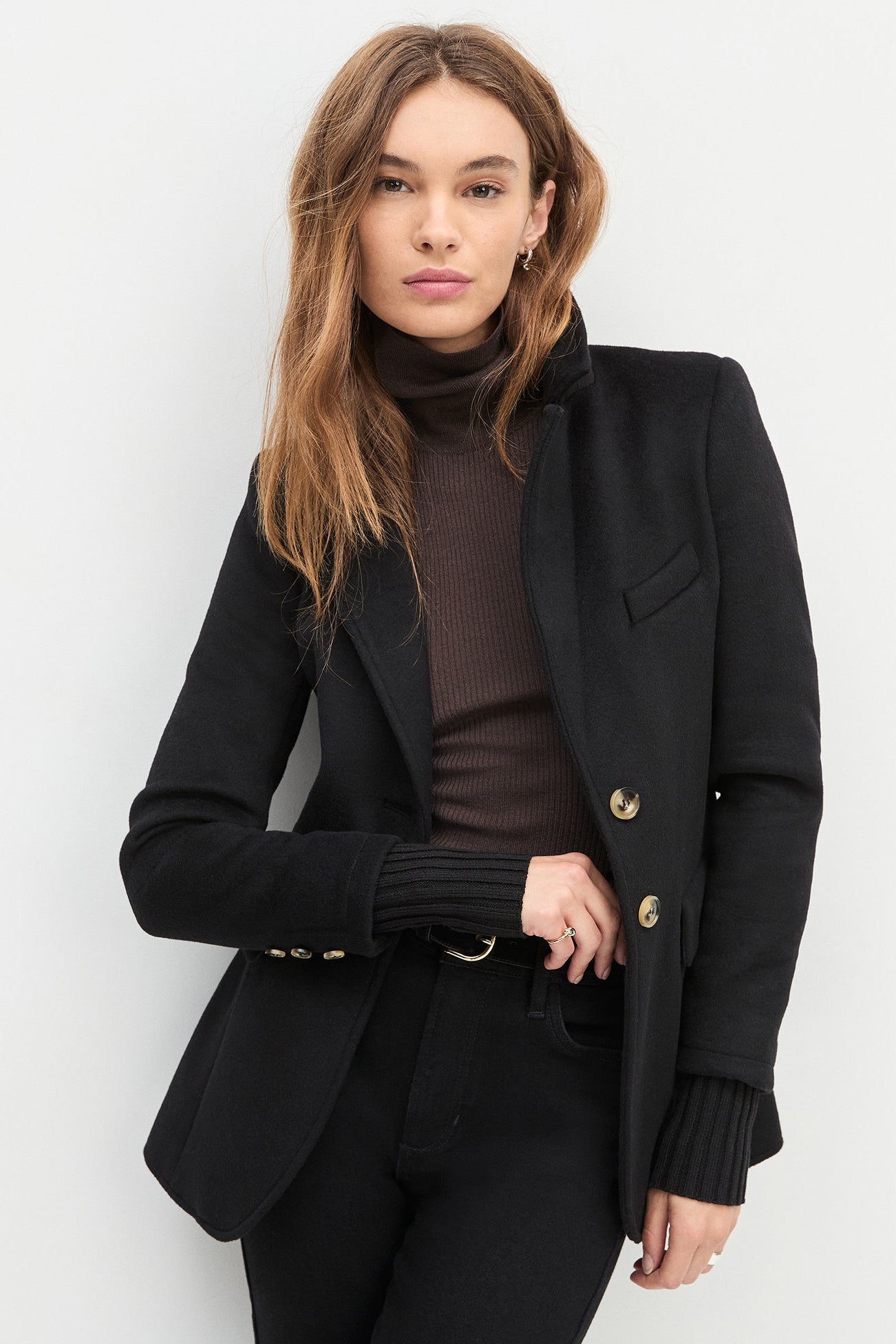 Woman wearing a black coat with gold buttons on a white background