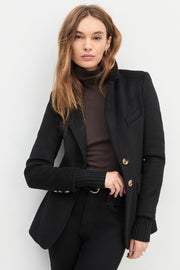 Woman wearing a black coat with gold buttons on a white background