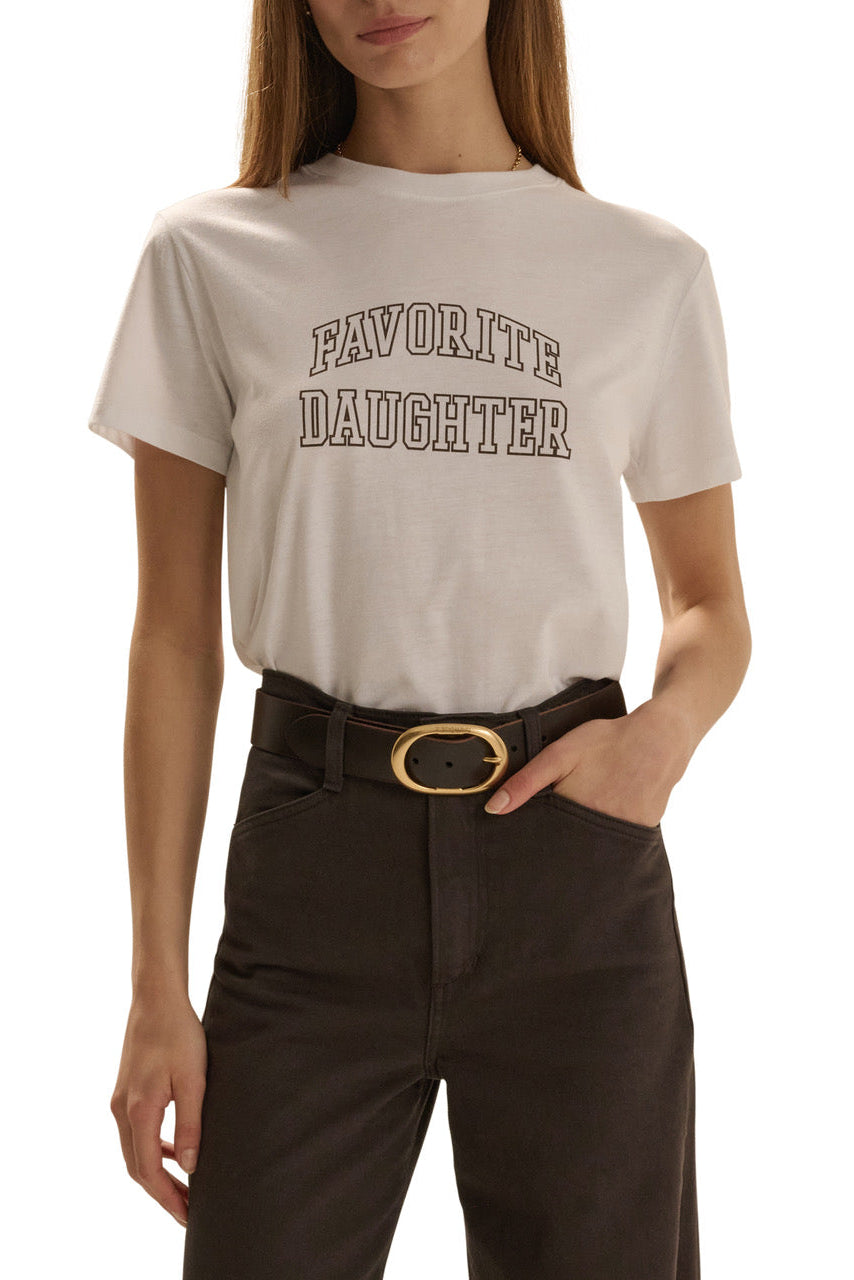 A woman wearing a cream-colored graphic t-shirt with 'FAVORITE DAUGHTER' printed in brown varsity-style lettering