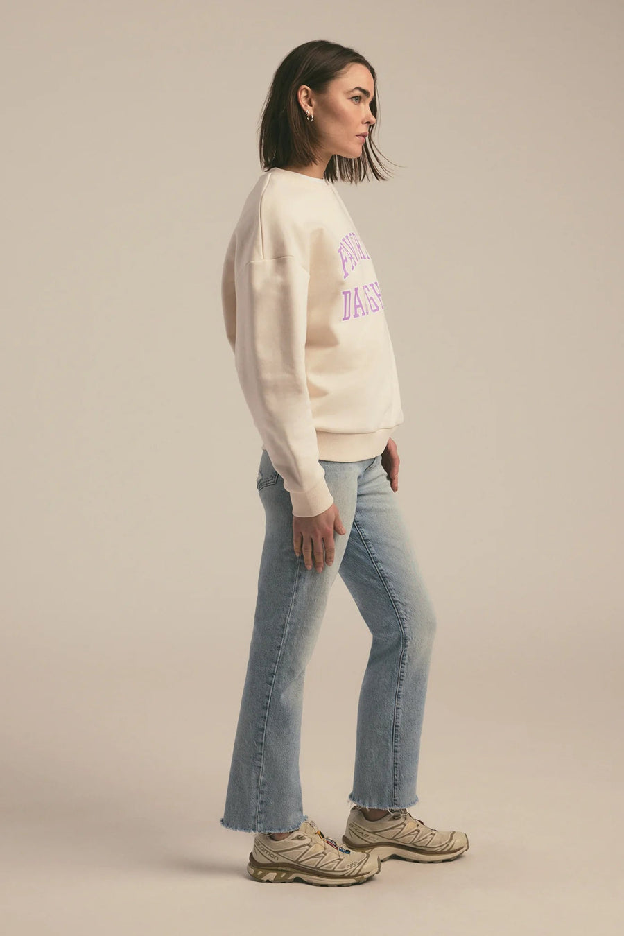 Person wearing a cream sweater with text and light blue jeans on a beige background