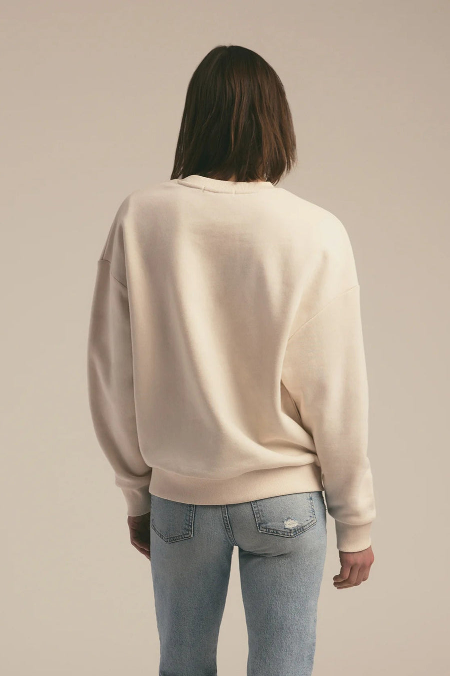 Person wearing a beige sweater and light blue jeans against a beige background