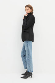 Side view of a woman wearing a black jacket with cuff sleeves, brown top and black jeans