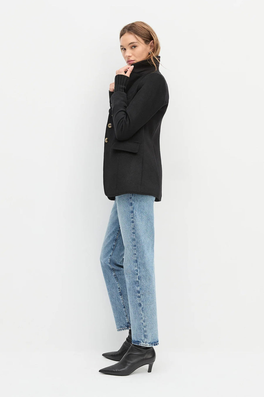 Side view of a woman wearing a black jacket with cuff sleeves, brown top and black jeans