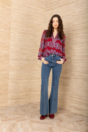 Full body view of woman wearing a red background and blue patterned long sleeve blouse tucked into blue jeans