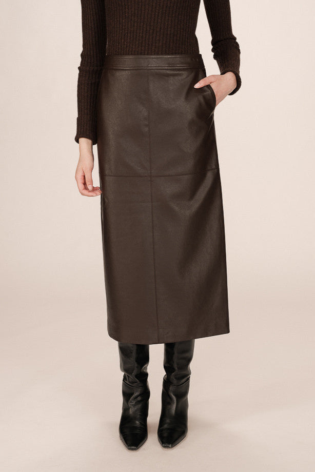 Front view of a person wearing a brown leather skirt and black boots on a beige background