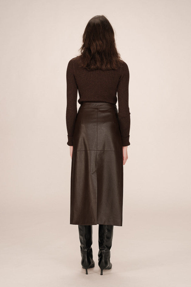 Back view of a person wearing a brown leather skirt and black boots on a beige background