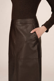 3/4 zoom in view of a person wearing a brown leather skirt and black boots on a beige background