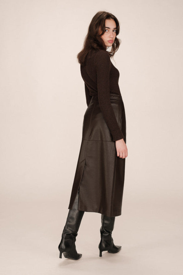 Back view of a person wearing a brown leather skirt and black boots on a beige background