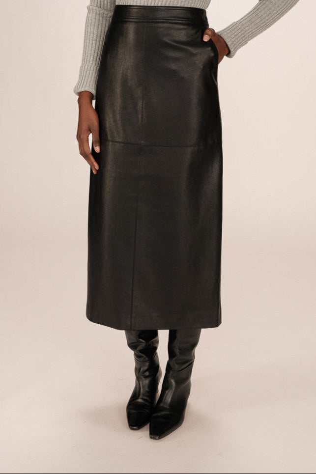 Front view of a person wearing a black leather skirt and black boots on a beige background