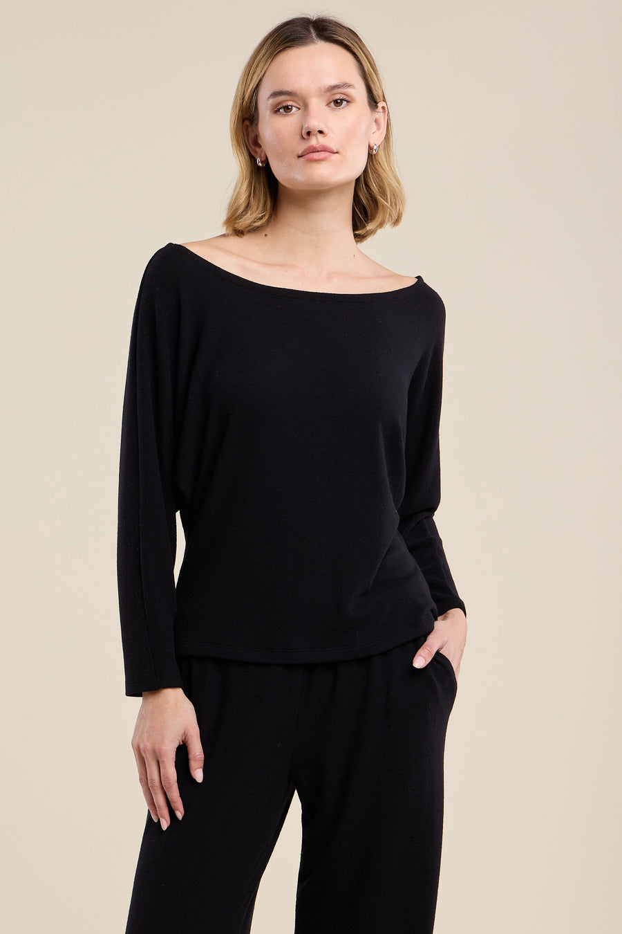 A woman modeling a black long-sleeve knit top with a wide boat neckline